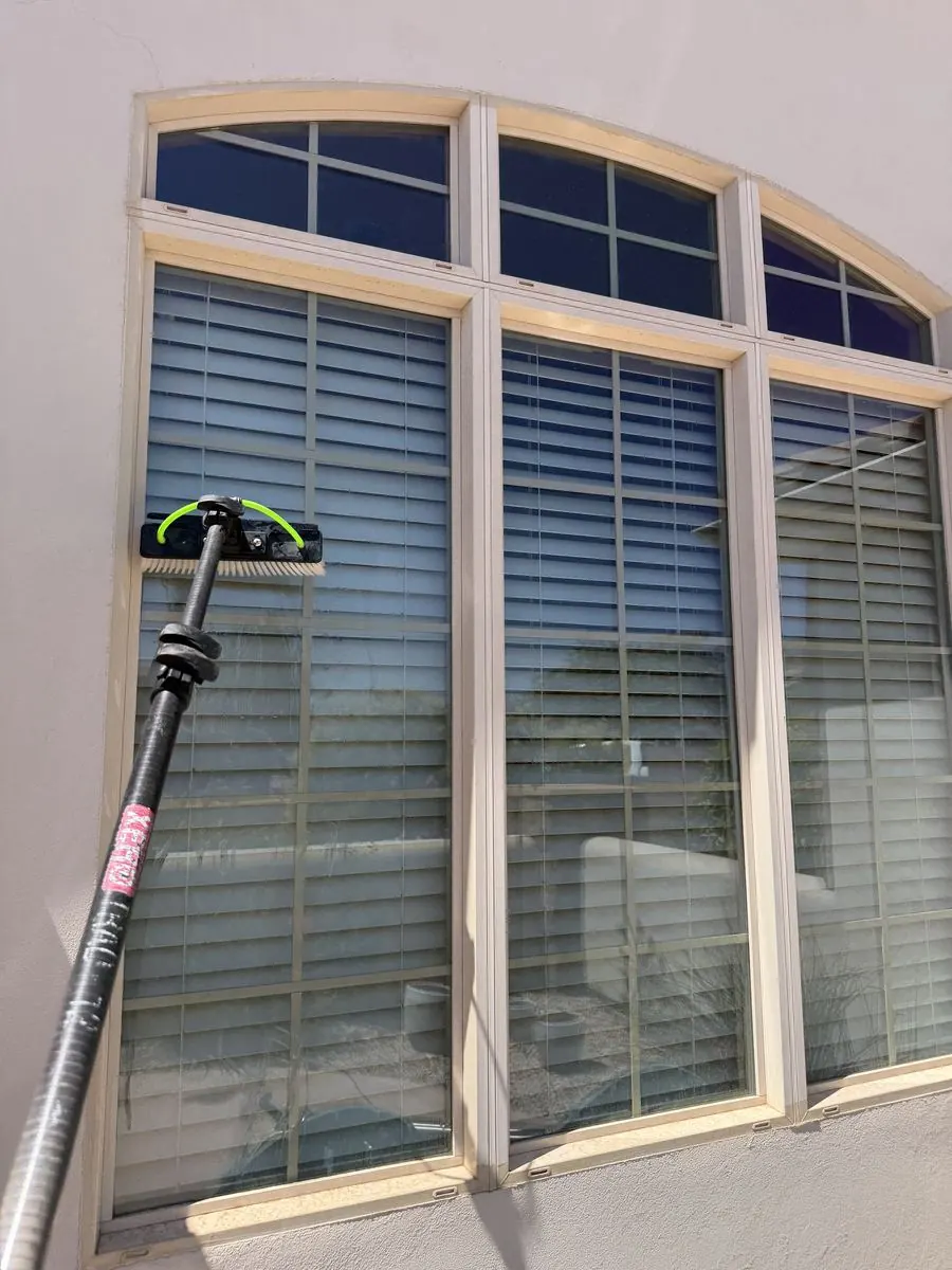 Technician cleaning a second-story window from a rooftop balcony