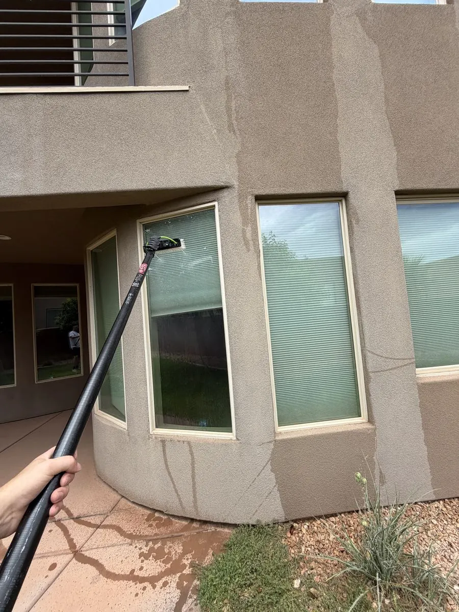 Technician cleaning a second-story window from a balcony overhang